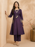 A woman models a deep purple three-piece Indian ethnic suit set consisting of a straight kurta, matching trousers, and a silver-toned chain necklace with a decorative pendant. The kurta features gold embroidery on the neckline, cuffs, and side pockets.