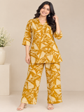 A woman modeling a mustard yellow and cream abstract print two-piece kurta set against a neutral beige background.